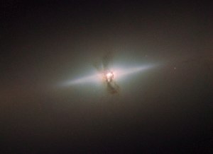 The elegant simplicity of NGC 4111, seen here in this image from the NASA/ESA Hubble Space Telescope, hides a more violent history than you might think. NGC 4111 is a lenticular, or lens-shaped, galaxy, lying about 50 million light-years from us in the constellation of Canes Venatici (The Hunting Dogs). Lenticular galaxies are an intermediate type of galaxy between an elliptical and a spiral. They host aged stars like ellipticals and have a disk like a spiral. However, that’s where the similarities end: they differ from ellipticals because they have a bulge and a thin disk, but are different from spirals because lenticular discs contain very little gas and dust, and do not feature the many-armed structure that is characteristic of spiral galaxies. In this image we see the disc of NGC 4111 edge-on, so it appears as a thin sliver of light on the sky. At first sight, NGC 4111 looks like a fairly uneventful galaxy, but there are unusual features that suggest it is not such a peaceful place. Running through its centre, at right angles to the thin disc, is a series of filaments, silhouetted against the bright core of the galaxy. These are made of dust, and astronomers think they are associated with a ring of material encircling the galaxy’s core. Since it is not aligned with the galaxy’s main disc, it is possible that this polar ring of gas and dust is actually the remains of a smaller galaxy that was swallowed up by NGC 4111 long ago.